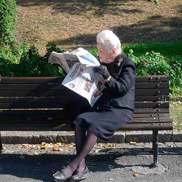donna anziana che legge il giornale al parco