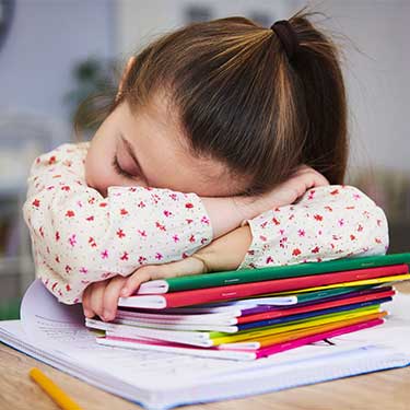 bambina addormentata a scuola con le braccia sui quaderni e la testa appoggiata sulle braccia